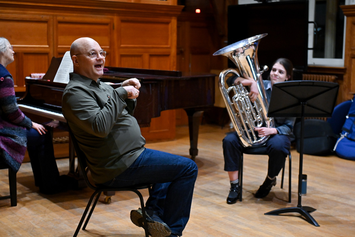 A male teacher instructing a class, with a female tuba player listening to him.